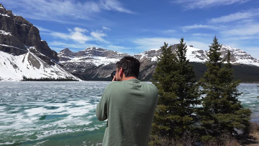 Man photographing frozen Bow lake mountains in Banff National Park