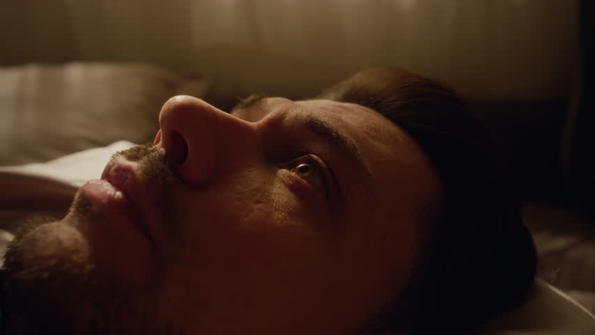 Close up of adult man with beard covering face with hands in despair lying on bed while going through emotional breakdown