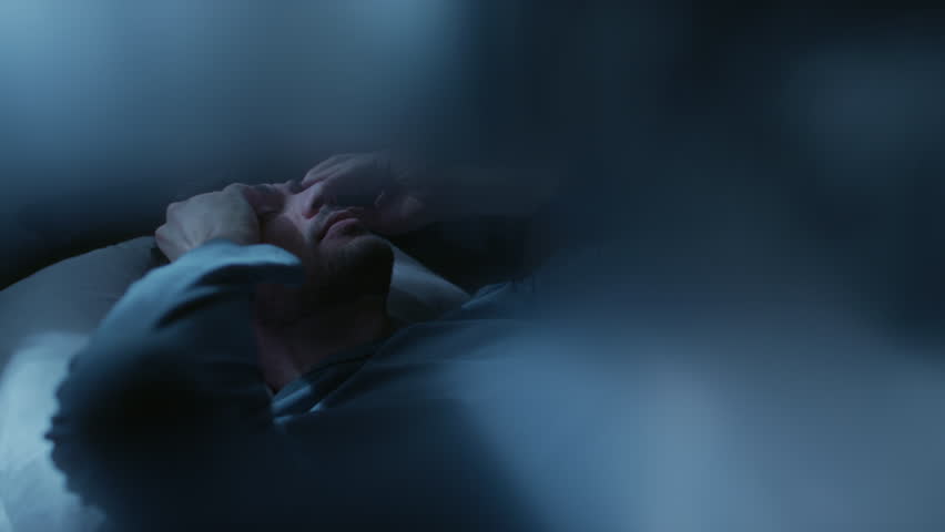 Adult man checking time on phone while tossing and turning in bed at night then getting frustrated in struggle to get to sleep, copy space