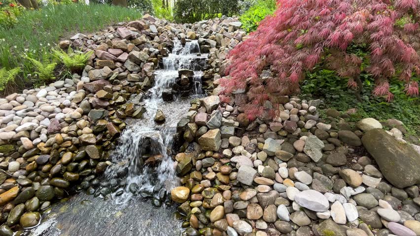 Crystal clear water stream running down stones in form of cascade at world famous Keukenhof tulip garden, peaceful spring scene from tourist attraction Dutch botanical park in Lisse, the Netherlands