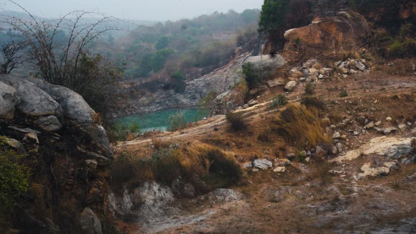 Rocky hillside landscape overlooking a turquoise quarry lake surrounded by rugged terrain and natural vegetation.