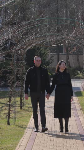 Vertical. Positive married couple walks joining hands under arch in spring park