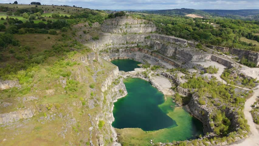 Aerial Cinematic View of Deep Blue Water at the Bottom of a Sunlit Derelict Limestone Quarry in the Scenic Derbyshire Dales, Peak District, UK
