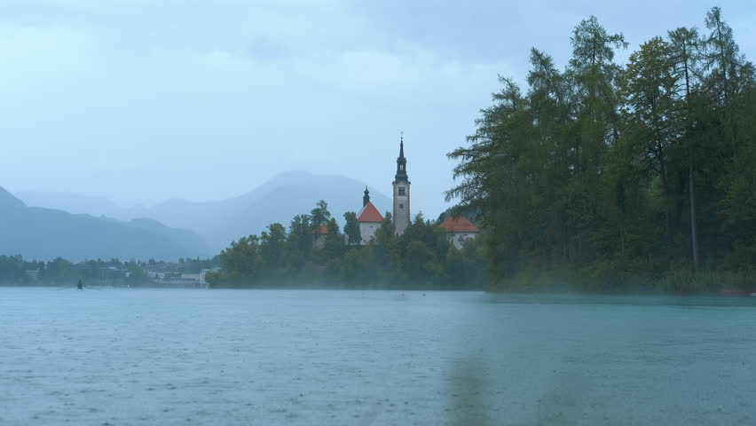 Rain falling on lake bled island with church in slovenia. Gentle rain falls on lake bled, creating ripples on the water's surface, with bled island and its iconic church visible in the background