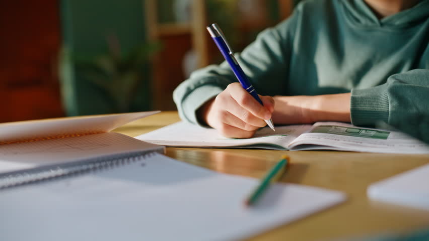 Schoolboy hands writing homework domestic workplace closeup. Serious little boy holding pen make notes copybook learning subject home. Attentive elementary school student studying lesson sitting desk.