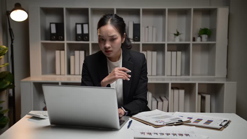 Young asian woman working on a laptop computer during overtime in a modern office at night