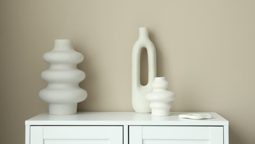 Man putting vase onto cabinet near beige wall indoors, closeup