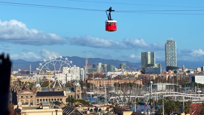View of Port Vell harbor with the red cable car, Port Cable Car, crossing, the Ferris wheel, and city skyline in Barcelona, Spain
