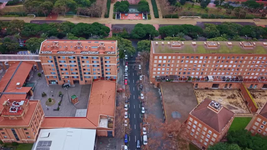 Top down drone glide between residential buildings in Vila Olímpica del Poblenou Barcelona revealing the green axis and Parc de la Nova Icària urban park layout.