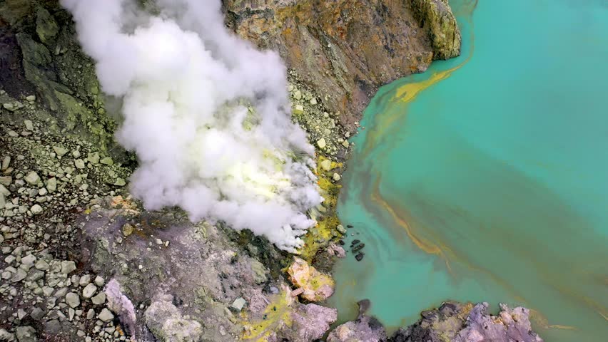 Aerial Drone Shot Looking Down at Active Crater Volcano. Contrast Between Turquoise Acidic Water and Yellow Sulfur Rocks. Above View on Shore Of Kawah Ijen Volcano In East Java Indonesia at Summer 4k