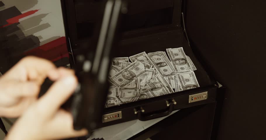 a handgun in front of an open briefcase filled with cash. Concept of robbery, organized crime, extortion, illegal money, and criminal activity.