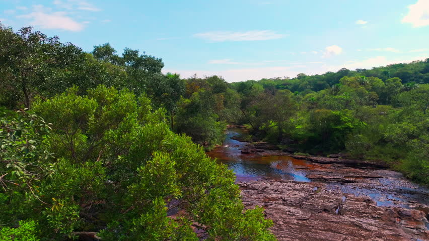 Drone footage of the colorful Caño Sabana river highlights bright natural tones, tropical vegetation, and the remote landscape of Guaviare, Colombia.