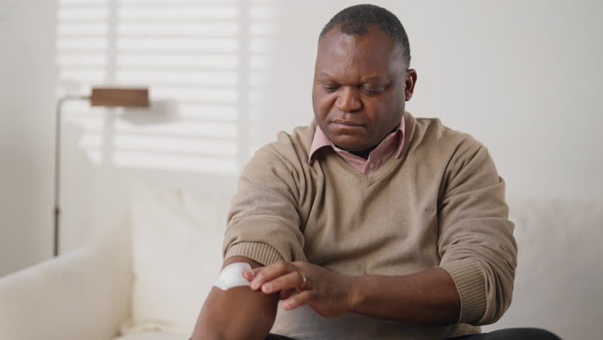 Portrait of middle-aged man unpacking and sticking nicotine patch on arm. Innovative transdermal patch for curing nicotine addiction and inputting medicine in blood, modern technology of medicine