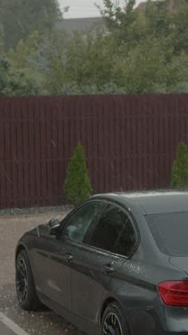 Vertical Screen: Rain and hail fall heavily in a city parking lot, creating a dramatic scene as icy pellets accumulate on the ground and vehicles during the storm.