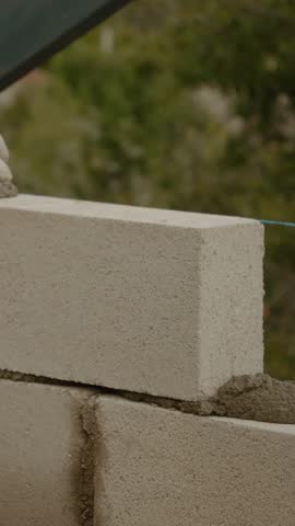 Vertical Screen: A worker skillfully builds a sturdy wall using concrete bricks to contribute to a new house construction project. Focus on craftsmanship and attention to detail.