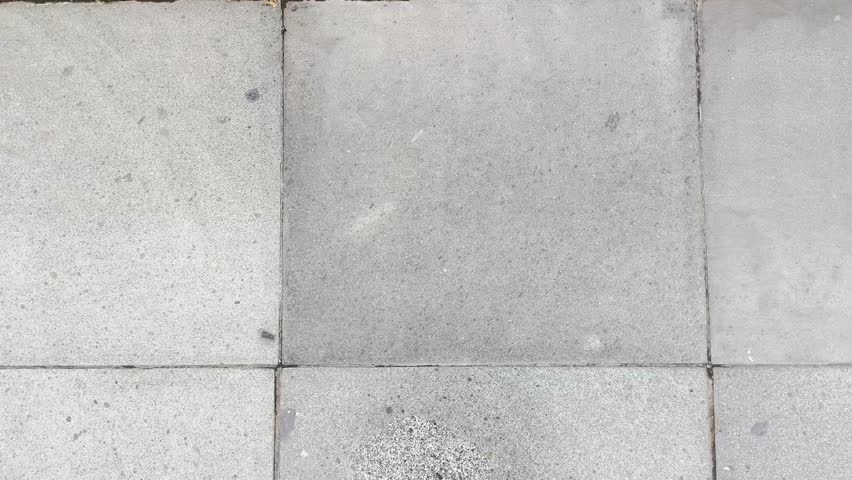 A smooth vertical camera movement (tilt-up) starting from a grey tiled floor to a large brown wall featuring white 3D Kufic Arabic calligraphy, ending with a view of the bright sky