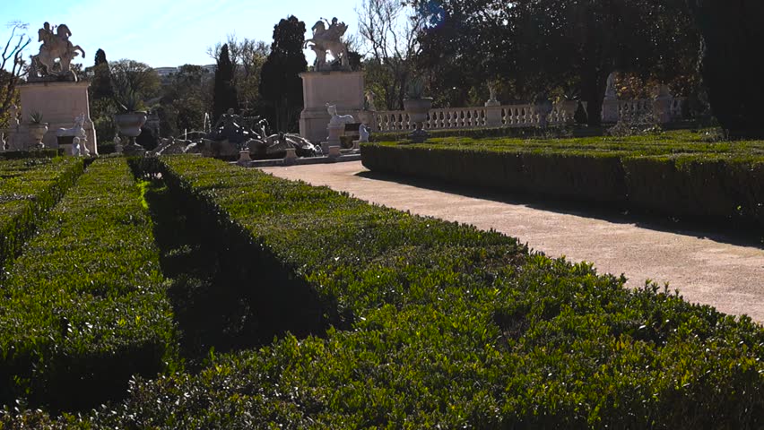 Wide view of geometric hedges and pathway leading toward the Neptune fountain in the formal gardens of Queluz National Palace in Portugal.