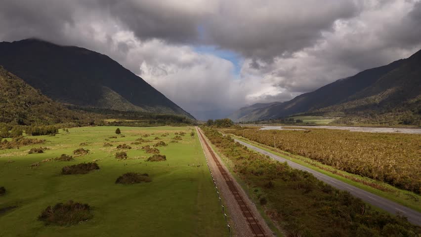 Drone flight over empty road and train tracks running through remote mountain valley in New Zealand. Aerial forward, copy space