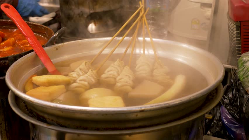 Slow motion close up of Eomukguk Odeng soup broth with skewered fishcakes cooking in large pot filled with hot water at Gwangjang street food night markets in Seoul city South Korea Asian cuisine