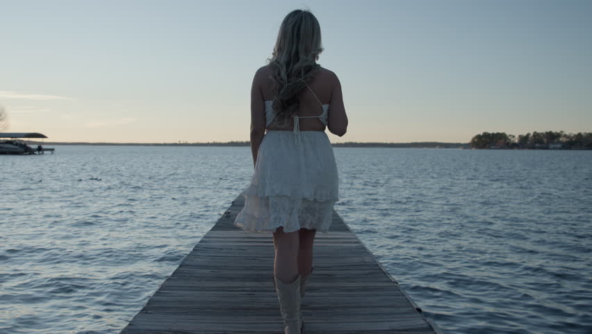 Beautiful blonde girl walking down a boat dock at sunset