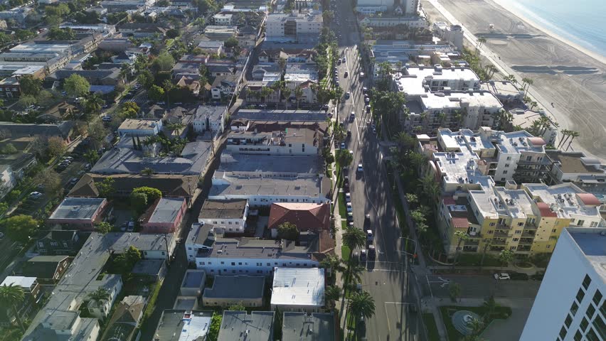 Beachfront residential edge Alamitos Beach with Ocean Blvd running parallel shoreline, modern apartments facing sand. Bright coastal light, rooflines, palms, reflective surfaces, Long Beach, CA. USA