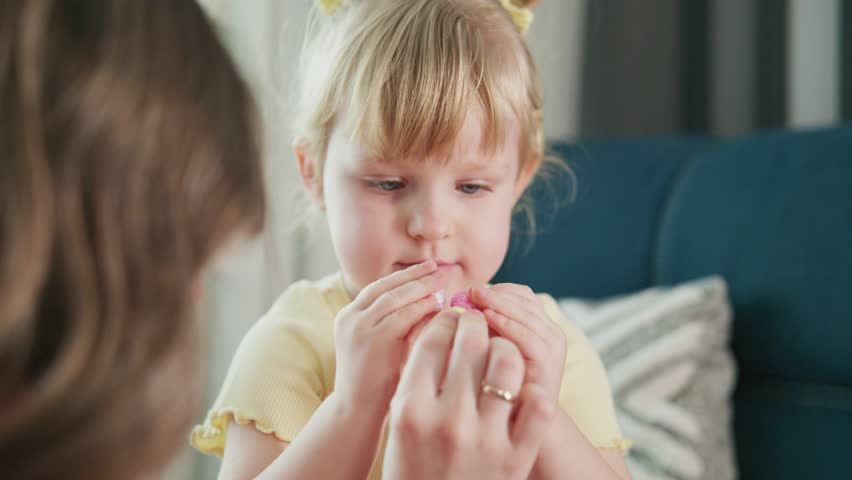 Young girl in yellow shirt sits on blue couch. She bites her nails nervously while looking down. Mother