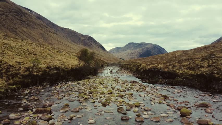 Dramatic Aerial View of Rocky River in Scotland, Aerial shot of a winding river flowing through a rocky mountain pass in the dramatic Scottish Highlands
