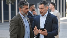 Two colleagues businessmen are discussing work looking at a mobile phone app - Powered by Shutterstock - Get 15% off with code: PIKWIZARD15