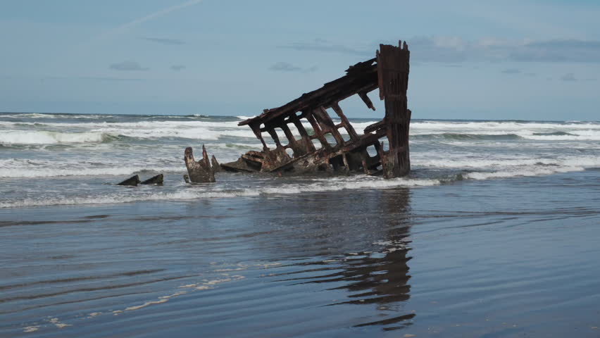 The rusted remains of a historic shipwreck emerge from the surf along the Oregon coast as waves crash against the skeletal hull.