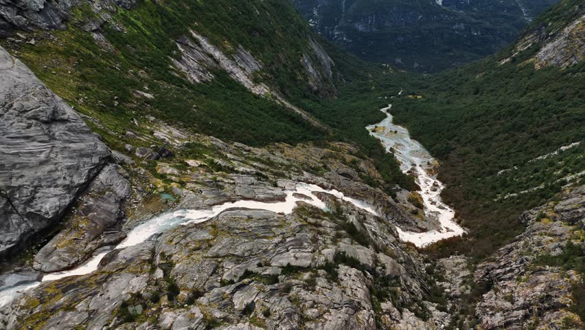 Dramatic waterfall cascading over moss-covered rocks in steep valley with green slopes, Norway, drone