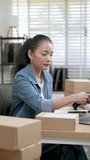 Asian woman small business owner scans shipping label on parcel box in vertical workspace, verifies order information, manages online selling process and prepares package for delivery workflow - Powered by Shutterstock - Get 15% off with code: PIKWIZARD15