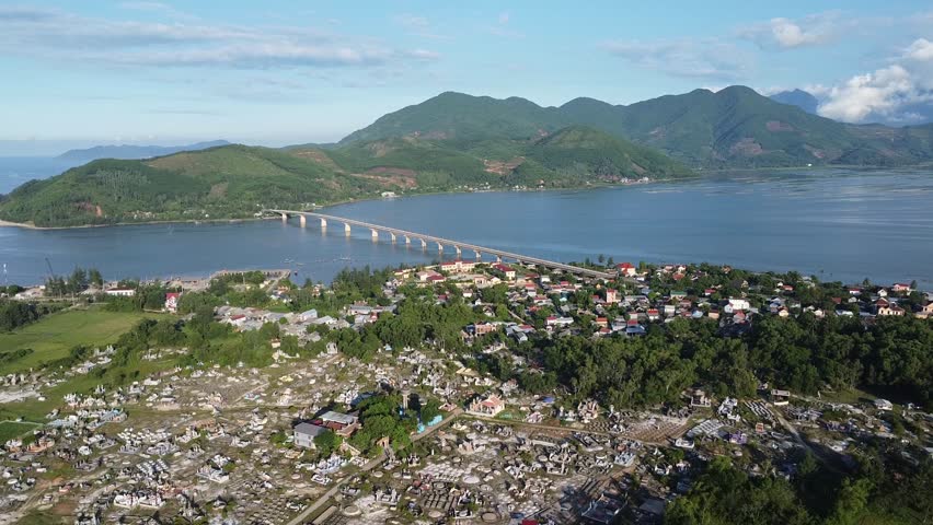 Aerial drone view of Da Nang coastal city with long bridge crossing wide bay surrounded by mountains and urban buildings along central Vietnam shoreline