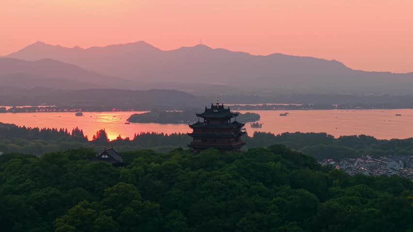 Aerial view of Chenghuang pagoda at sunset over Xihu lake in Hangzhou featuring mountains and lush green trees