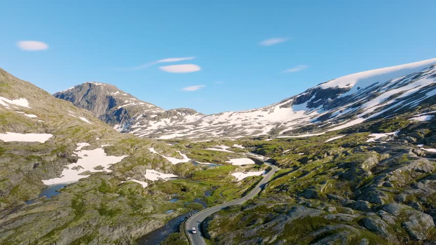 Aerial panoramic view of a winding road through rugged Norwegian mountains. Scenic highway among rocks and fjords under bright daylight. Summer travel destination and arctic wilderness in Norway