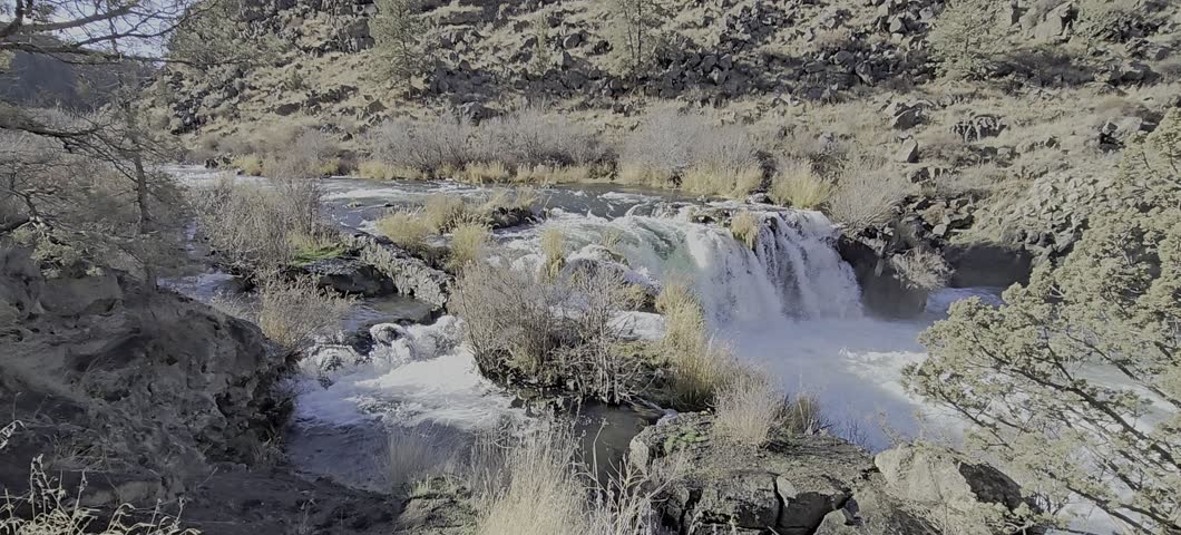 The video shows Steelhead Falls on the Deschutes River in Central Oregon. Located near Crooked River Ranch and Terrebonne, approximately 45 minutes from Bend. 
 The waterfall is a 20-foot drop spreading horizontally across a basalt ledge. The area is popular for hiking a family-friendly 0.5-mile trail, fishing, and cliff jumping into the canyon pool below. The area is surrounded by a canyon with colorful rimrock, juniper trees, and sagebrush. 
