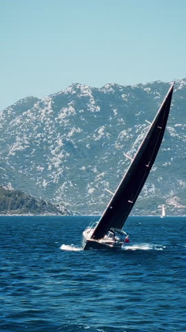 Close-up of elegant sailing yacht cruising through deep blue waters against rocky cliffs in background. Mugla, Turkey