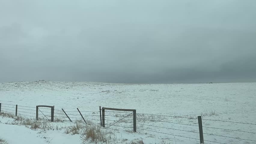 Snow covered prairie farmland with rolling fields and overcast sky in winter landscape