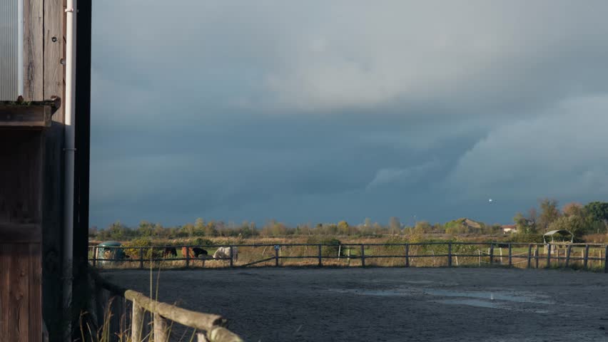 Horse paddock and rural landscape under dark storm clouds after rain. Quiet countryside scene with fences, fields, and dramatic sky creating a moody natural atmosphere.