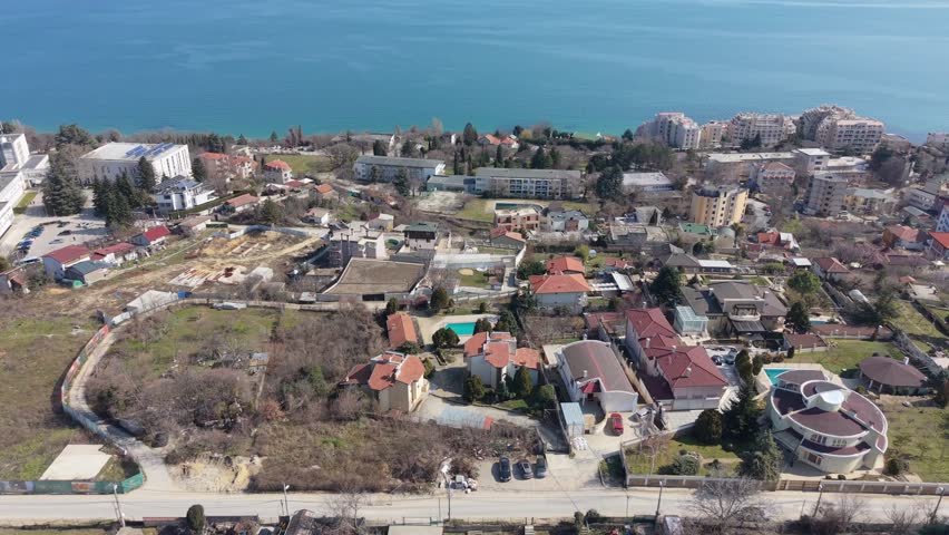 Aerial drone view of coastal city with residential buildings, shoreline road and beautiful blue sea landscape.