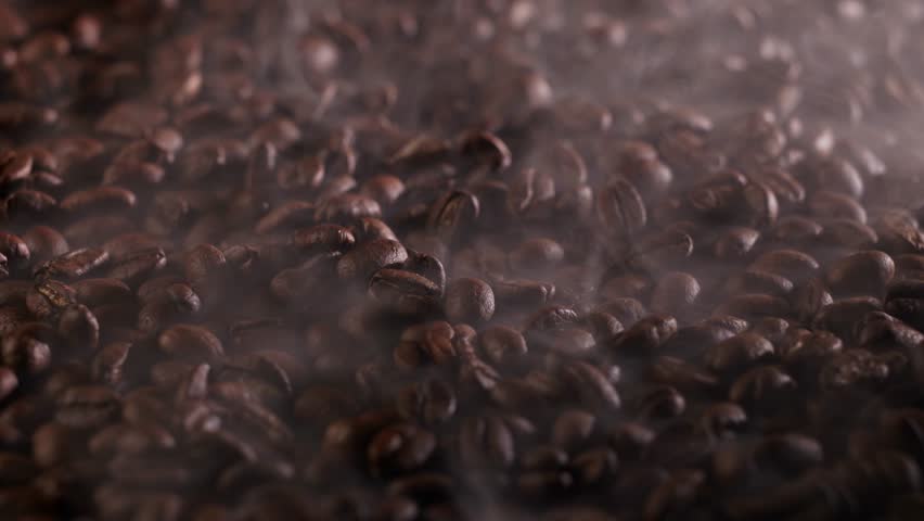 Slow motion roasted coffee beans smokeing on tabletop close up studio tracking shot.