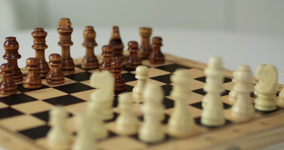 Hand moves chess piece on wooden board. Player plans strategy in intellectual chess game. Focus remains on figures during match. Logic guides every chess move for victory. Smart hobby improves mind.