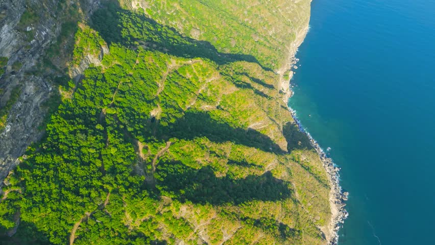 Aerial view of steep green cliffs and rocky shoreline of Jabal Shaat overlooking the Arabian Sea on the border between Oman and Yemen.
