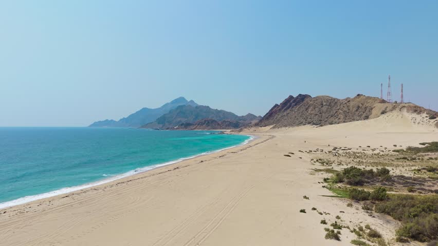 Aerial view of the sandy shoreline meeting turquoise ocean water and rugged desert mountains on Socotra Island, Yemen.