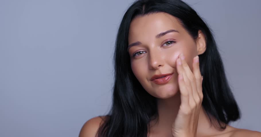 Close-up shot of young woman gently touching face with hand, showcasing radiant glowing skin and natural beauty. Perfect for cosmetics advertising and skincare campaigns.