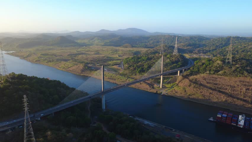 Centennial Bridge spans the Panama Canal with a cargo ship passing underneath.

Centennial Bridge and cargo ship in transit at the Panama Canal with Golden Morning Light showing a beautiful natural landscape around. A powerful combination of maritime trade, global logistics, and Panama’s natural landscape.