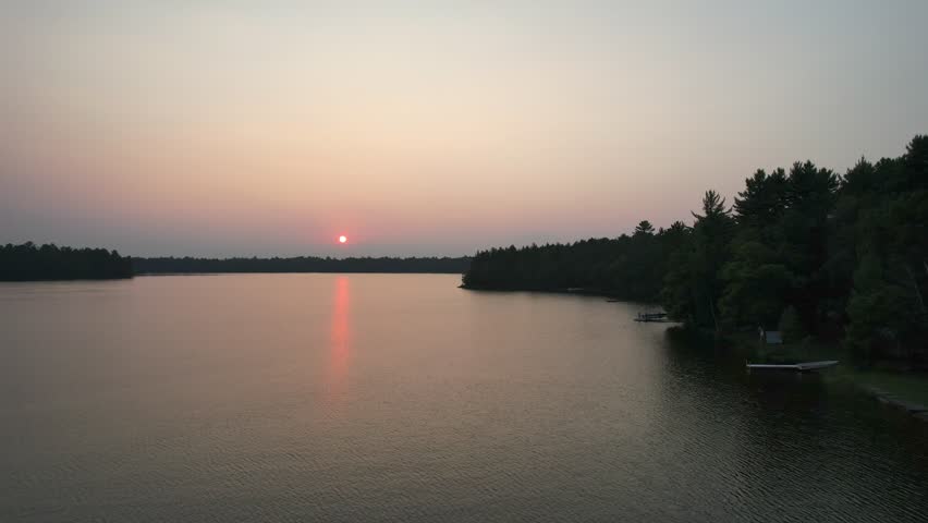 Aerial view of Eagle River Wisconsin in the Northwoods during summer.  Low drone approach shot with Red sun in the background at dusk.