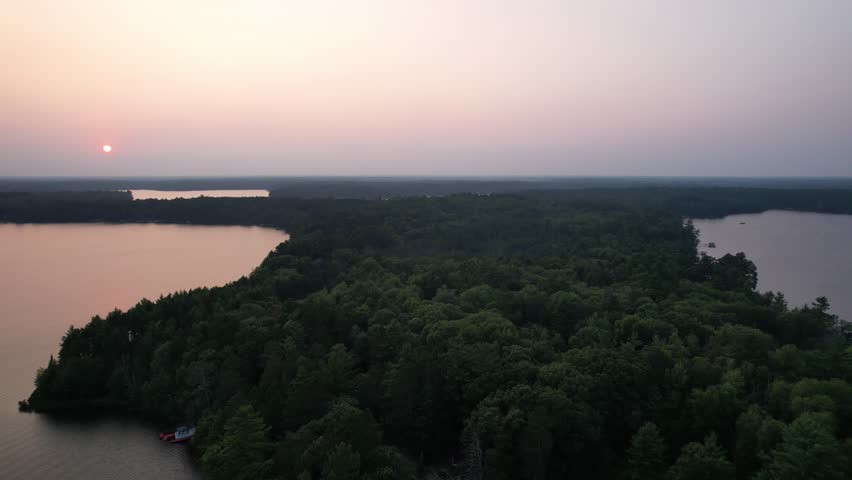 Aerial view of Eagle River Wisconsin in the Northwoods during summer.  Approach drone shot of lake country with pink sky.