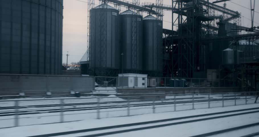 Winter Train Journey Past Industrial Silos and Snowy Landscape