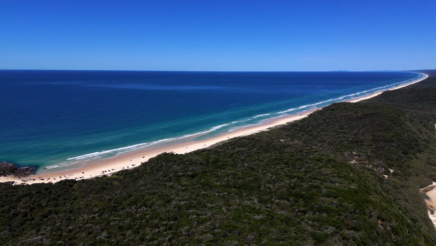 Aerial view of Rainbow Beach in Queensland, Australia with turquoise ocean, sandy coastline, coastal lagoon and large sand dunes.