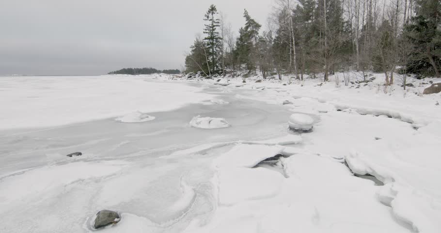 Wintry scene at Kopparnäs frozen coastline, rocky, snow-covered shores and icy waters in cloudy winter weather, Degerby, Finland, Europe.